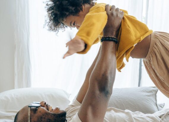 excited black father and cute son having fun on bed